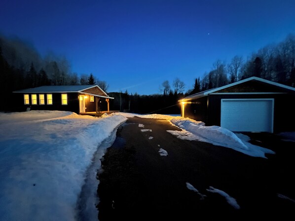 A two-story house with a garage, surrounded by snow-covered ground and trees.