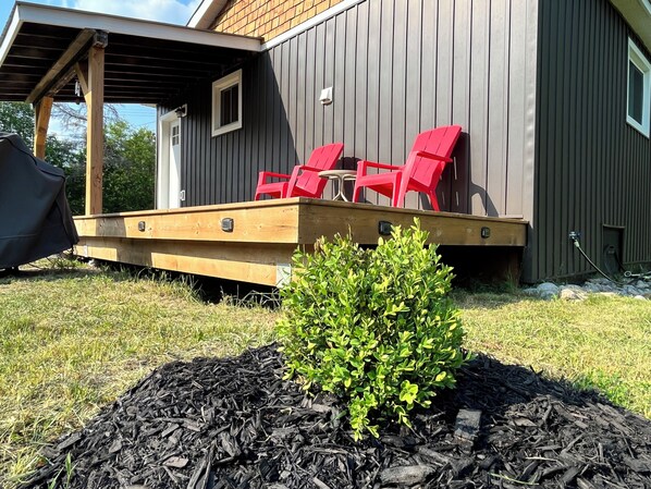 A wooden deck with red chairs, a small bush, and a building with vertical siding.