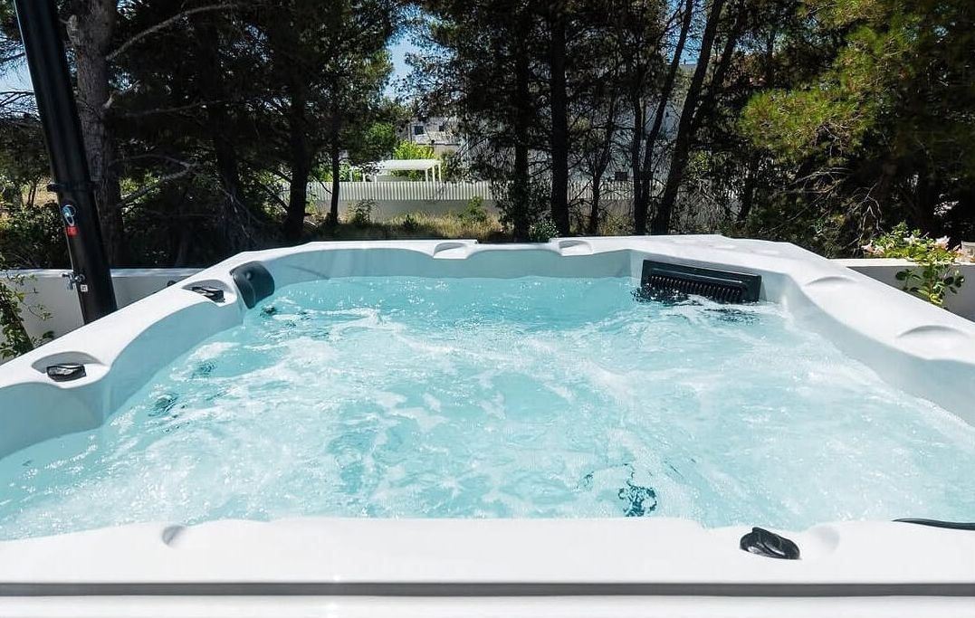 A hot tub in a garden setting with a view of a house in the background.