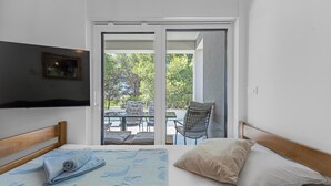 Een slaapkamer met een bed, een aan de muur bevestigde televisie en een schuifglazen deur naar een terras.