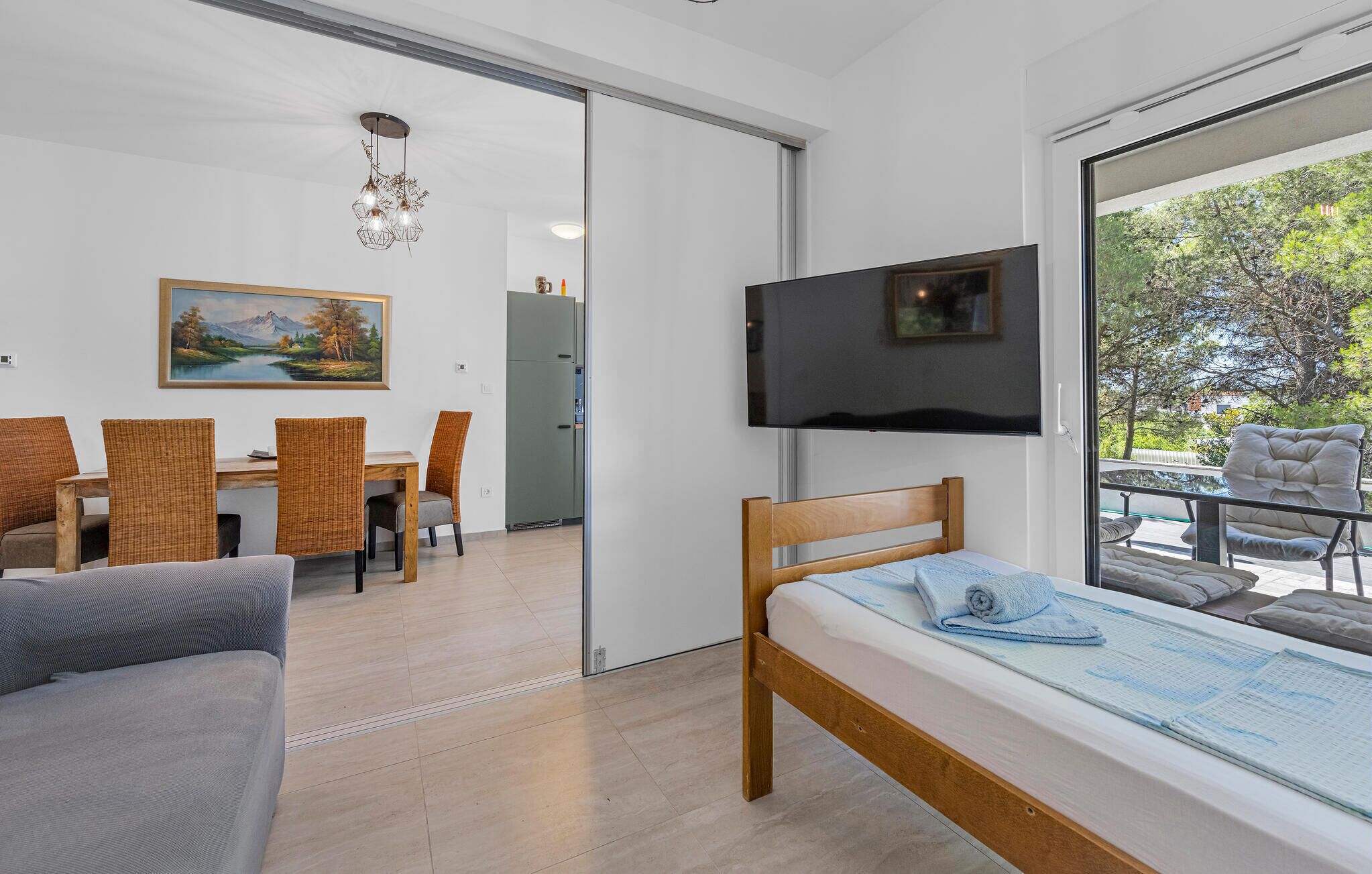 A modern room with a bed, a TV, a dining area with chairs, and a painting on the wall.