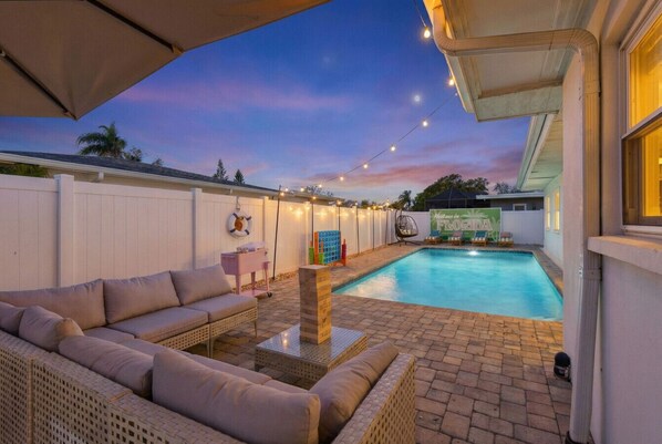 A backyard with a swimming pool, outdoor furniture, and string lights.
