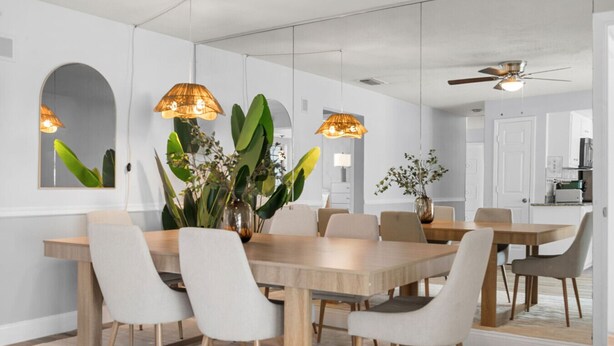 Un espace repas avec une table en bois, des chaises blanches et des lampes suspendues.