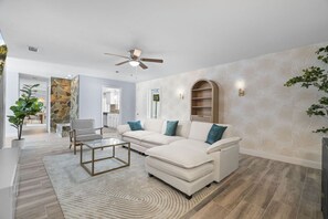 A modern living room with a sofa set, a coffee table, a stone accent wall, and a ceiling fan.