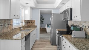 Une cuisine moderne dotée de plans de travail en granit, d’appareils électroménagers en acier inoxydable et de meubles blancs.