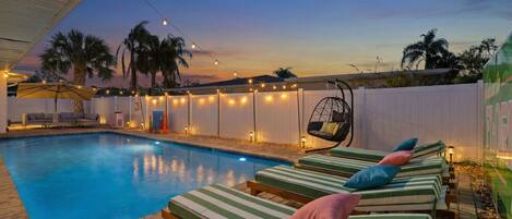 A swimming pool with lounge chairs and string lights.