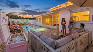 Un espace piscine avec des chaises longues, une glacière remplie de boissons et un patio couvert.