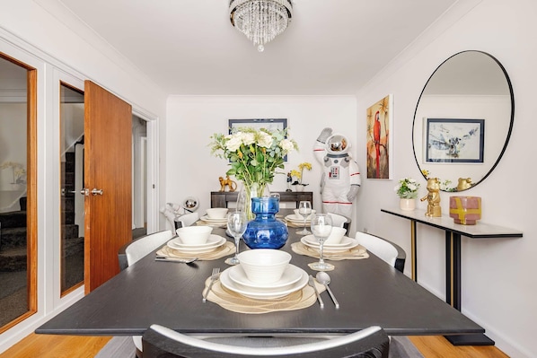 A dining room with a dark wooden table set for six, white plates, and a blue vase with flowers.