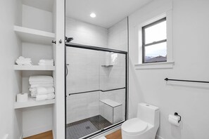 Une salle de bain moderne avec une douche à parois de verre, des carreaux blancs, des toilettes et une fenêtre.