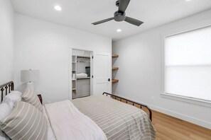 Une chambre à coucher comprenant un lit, un ventilateur de plafond, une fenêtre avec des stores et un placard avec des étagères.