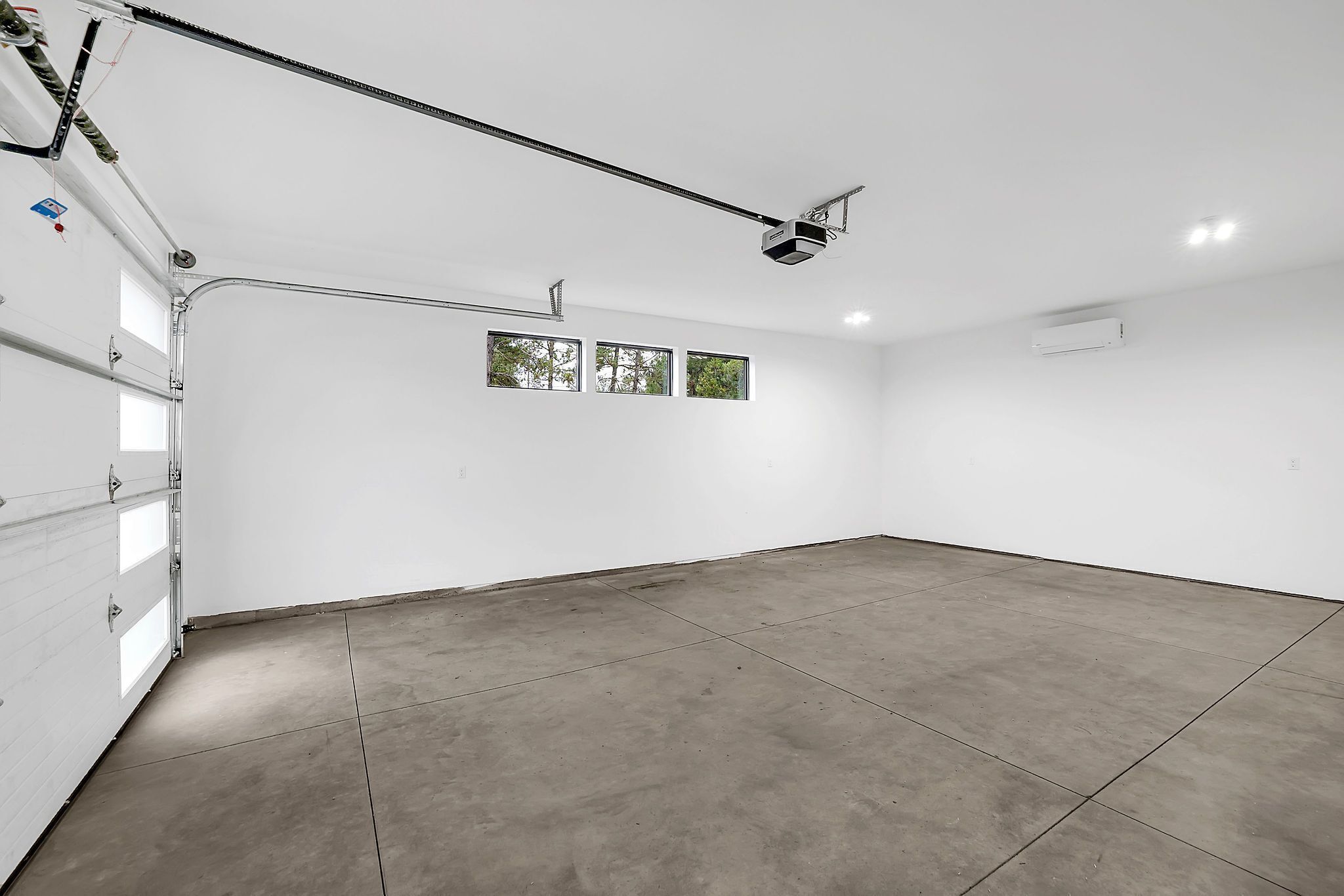 Eine geräumige Garage mit Betonboden, einer weißen Garagentür und einem an der Decke befestigten Projektor.