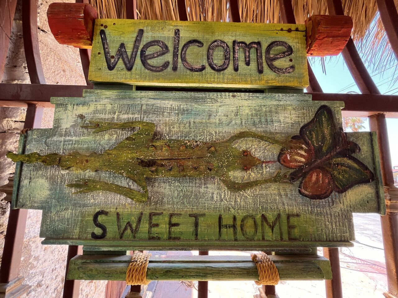 Un letrero de madera rústico con las palabras “Welcome” y “Sweet Home” sobre una rama con hojas.
