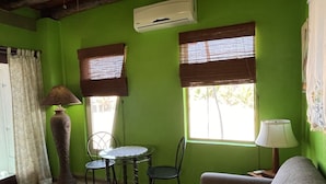 A room with green walls, a round table with chairs, a sofa, a lamp, and an air conditioning unit.