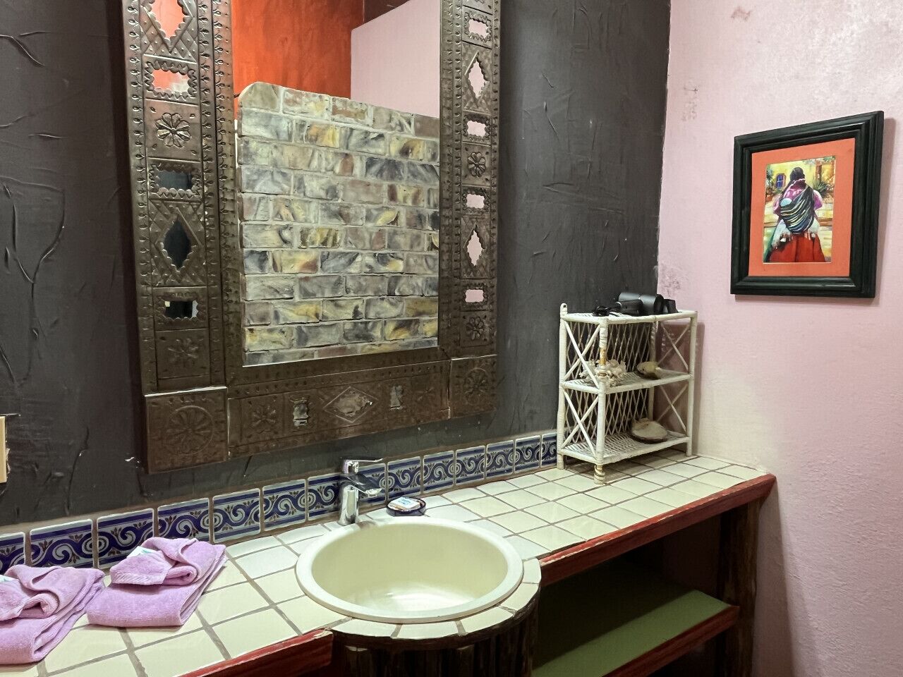Casa de banho com parede de pedra, pia branca, espelho e prateleira com sapatos.