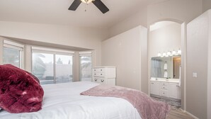 Een slaapkamer met een groot bed, een plafondventilator, een dressoir en een kaptafel met spiegel en verlichting.
