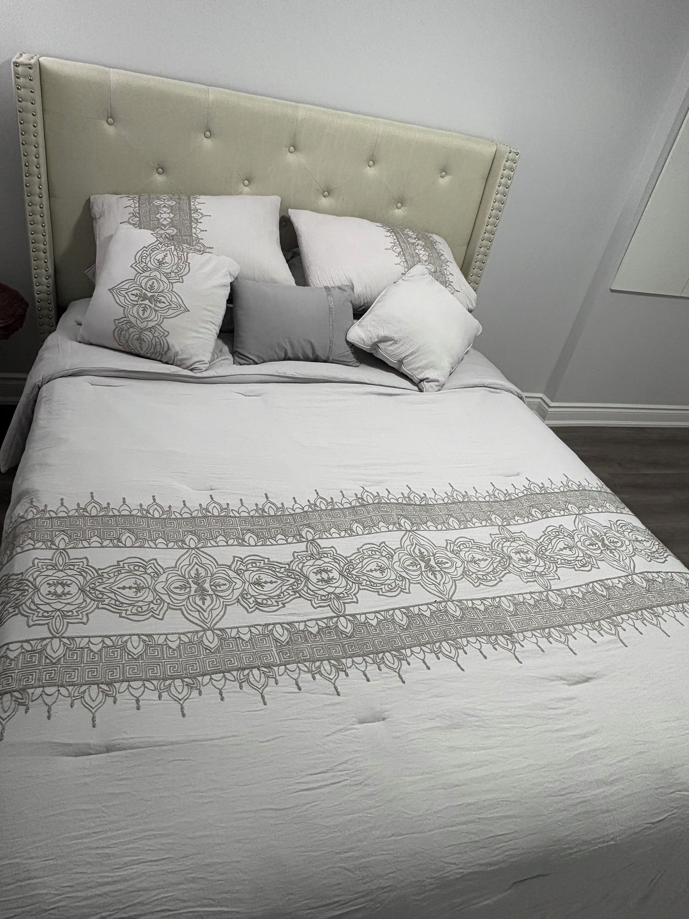 A bed with a tufted headboard, multiple pillows, and a patterned bedspread.