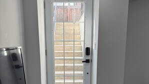 Ein heller, moderner Eingangsbereich mit einer weißen Tür, einem kleinen Podest, das zu einer Holztreppe führt, und einer Bank auf der rechten Seite.