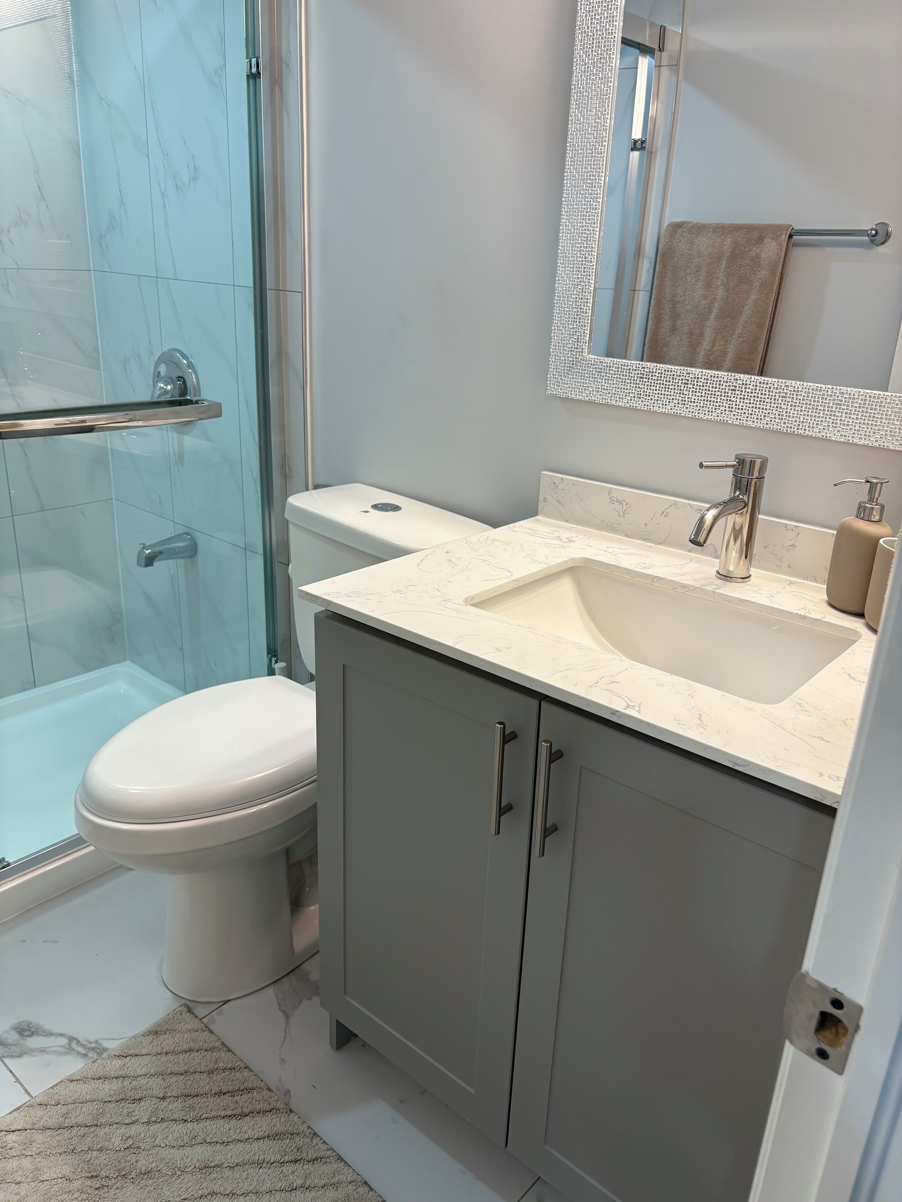 A bathroom with a glass shower enclosure, a toilet, a sink with a mirror above it, and a towel rack.