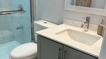 A bathroom with a glass shower enclosure, a toilet, a sink with a mirror above it, and a towel rack.