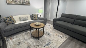 Ein modernes Wohnzimmer mit einem grauen Sofa, einem runden Couchtisch und einem gemusterten Teppich.
