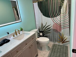 Une salle de bain avec un lavabo blanc, des robinets dorés, des toilettes blanches et un rideau de douche à rayures.