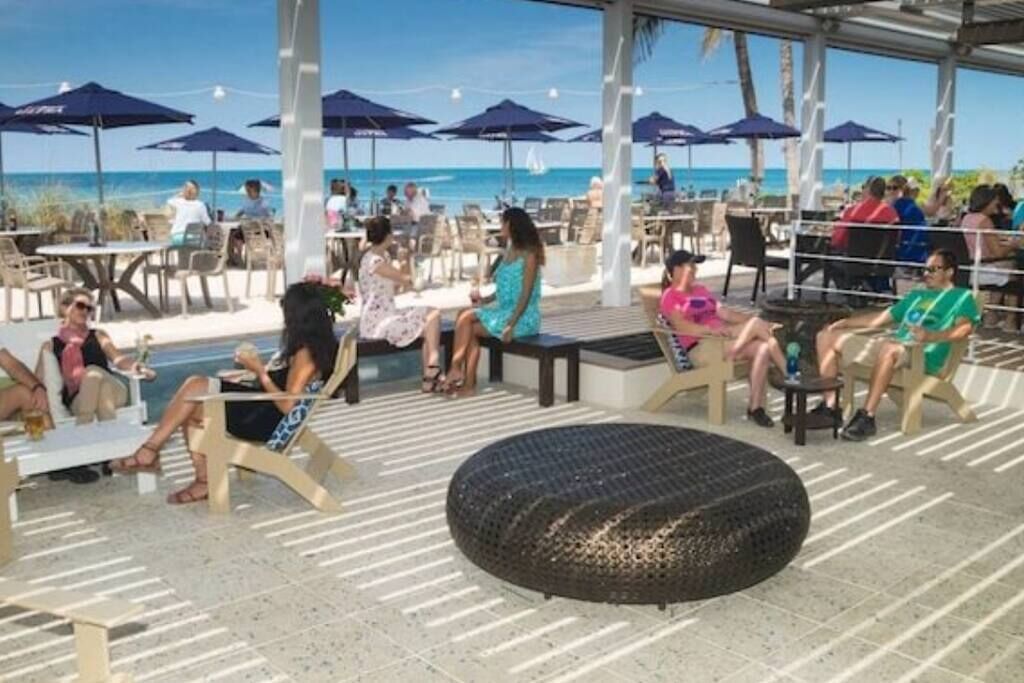 Área externa com mesas, cadeiras, guarda-sóis e vista para a praia.