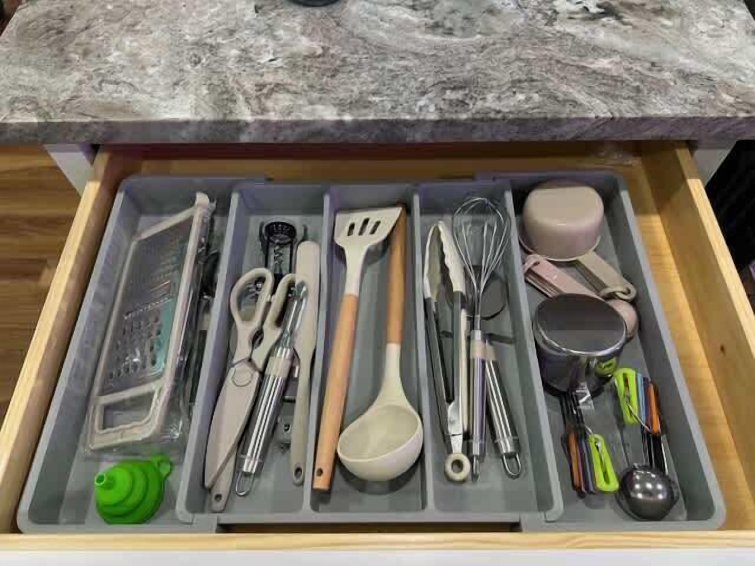 A drawer with kitchen utensils including a whisk, spatula, and measuring cups.