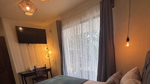 A hotel room with a bed, a TV, a table, and a window with curtains. - Oasis by Franklin villa #3 (Provincia de Alajuela)