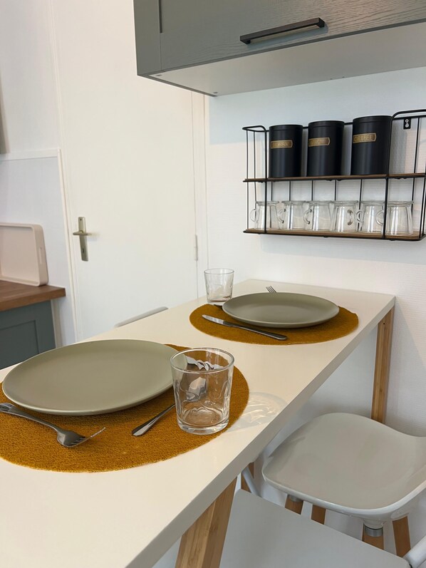 Una cocina con encimera blanca, dos platos, un vaso y un estante para cafetera.