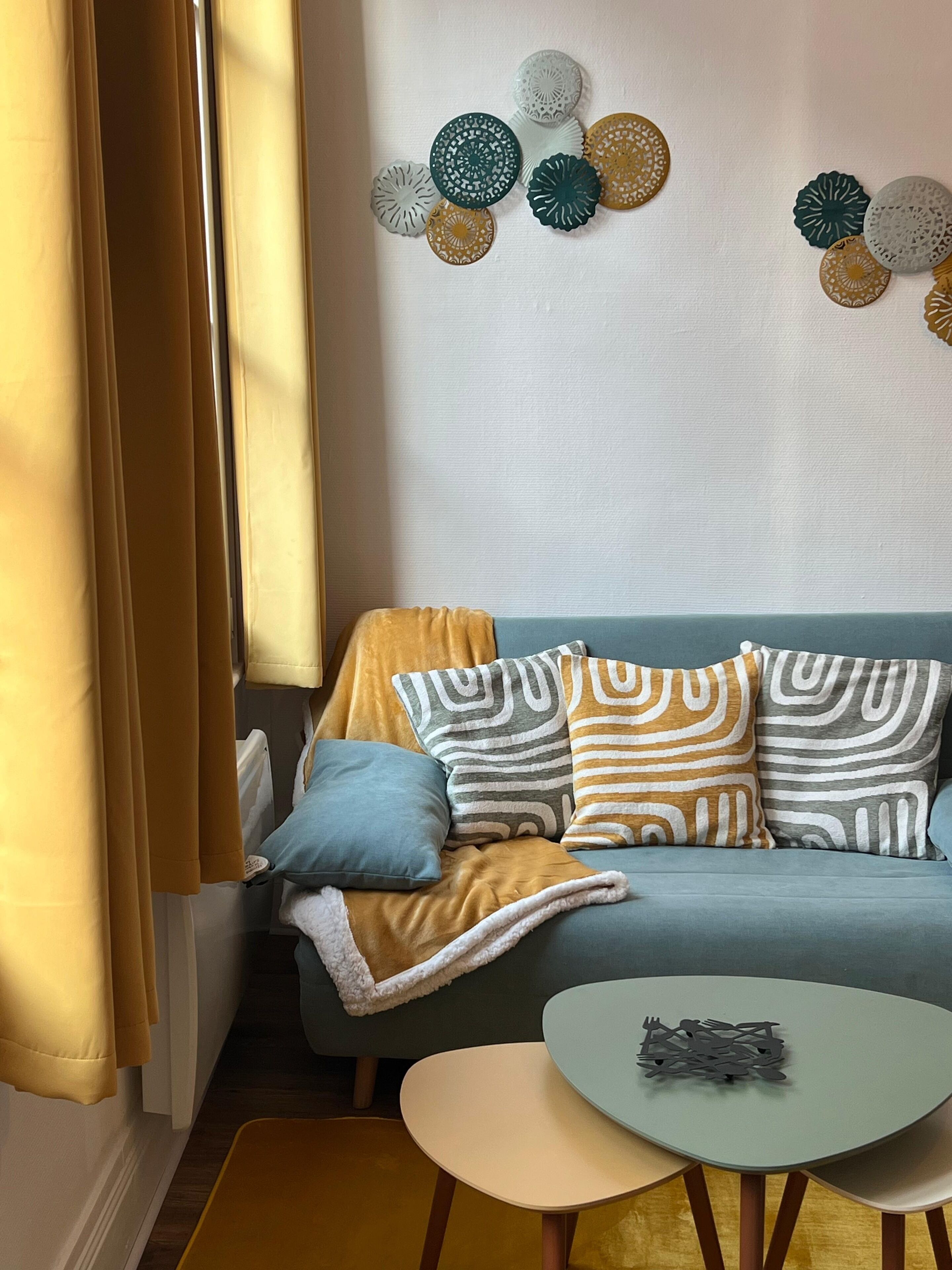 Un saló acollidor amb un sofà blau, coixinets estampats, una taula rodona petita i decoració mural.