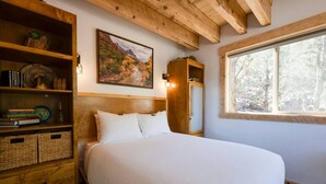 A bedroom with a bed, wooden headboard, a bookshelf, a painting, and a window.