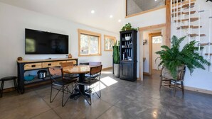 A modern living room with a dining table, chairs, a TV, a bookshelf, and a staircase.