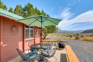 Un área de estar al aire libre acogedora con una mesa, sillas, un parasol verde y vistas del paisaje circundante.