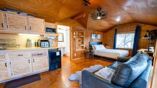A compact room with a kitchenette, a bed, a sofa, and a ceiling fan.