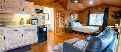 A compact room with a kitchenette, a bed, a sofa, and a ceiling fan.