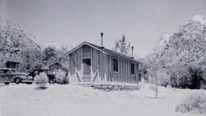 A wooden cabin with a gabled roof, two chimneys, and a front porch.