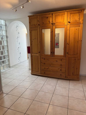 Ein hölzerner Kleiderschrank mit mehreren Schubladen und Türen, ein Fliesenboden und eine Glastür mit Dekor.