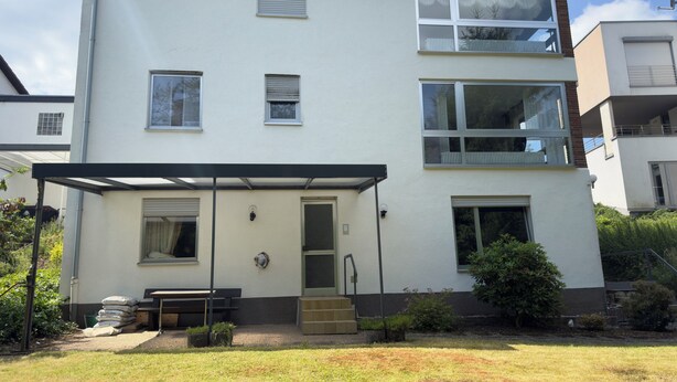 A two-story residential building with a covered patio, a front door, and a small garden area. - Spacious 130 m² Apartment ,3 Bedrooms, Garden & Parking  ,Sleeps 7 (Riegelsberg)