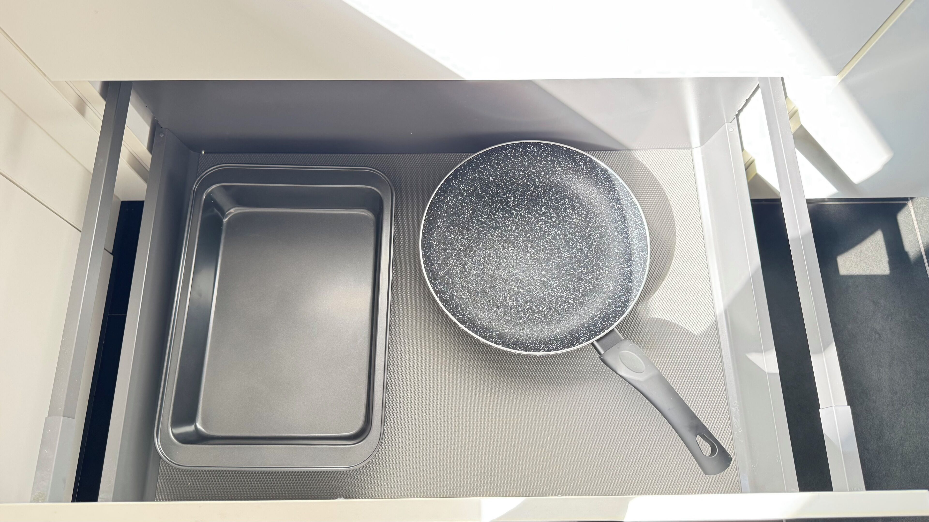 Un cajón de cocina con una bandeja metálica y una sartén antiadherente.