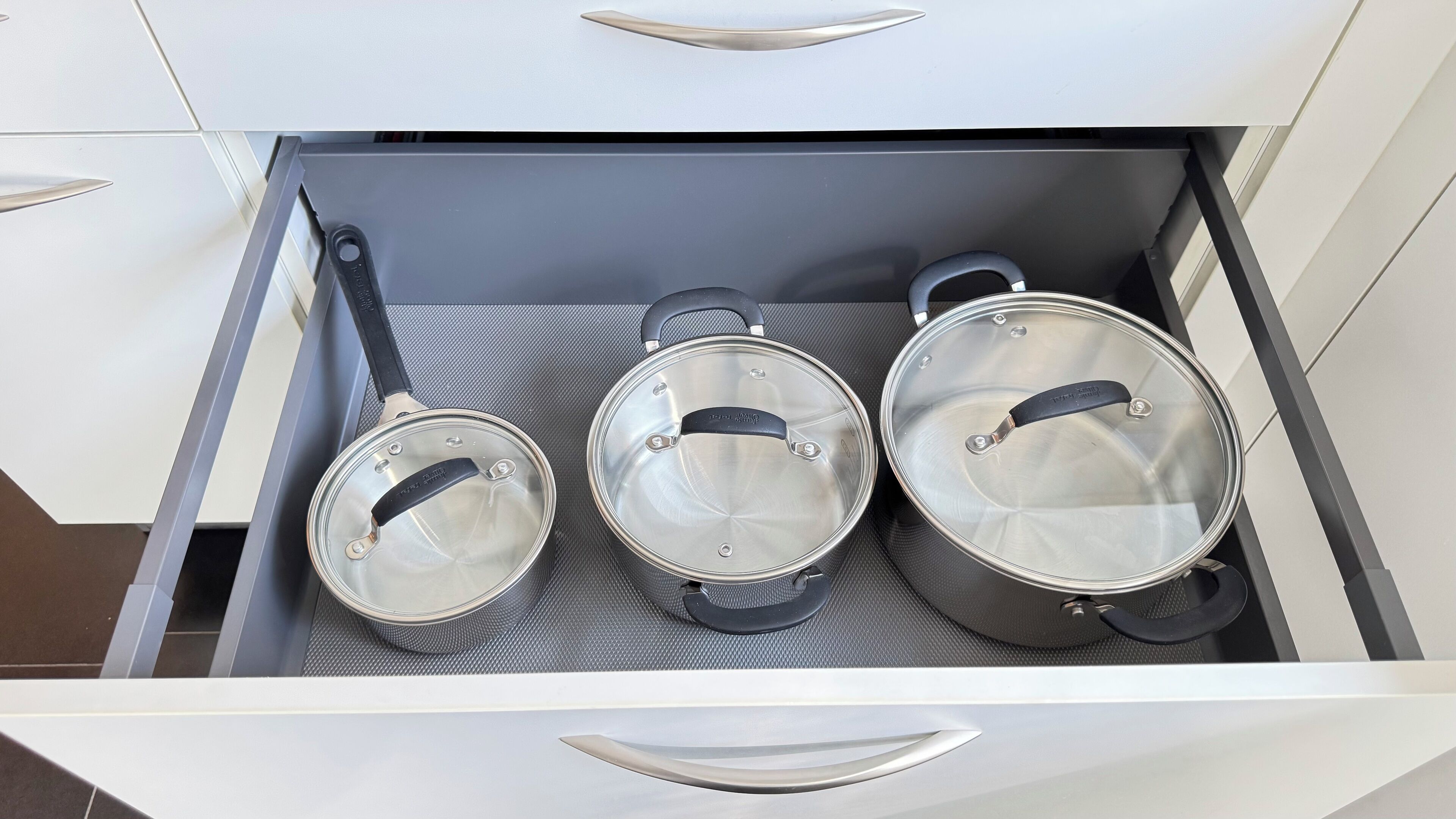 A drawer with three stainless steel pots with lids.