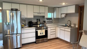 A compact kitchen with white cabinets, a stainless steel refrigerator, a stove, and a sink. - Stay At The Lake Cottage (Houghton Lake)