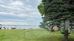 A grassy outdoor area with a swing set, a wooden bench, and a small table. - Stay At The Lake Cottage (Houghton Lake)