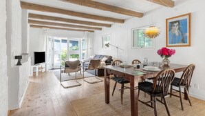 A dining area with a wooden table, chairs, and a vase of flowers. There is a sofa and a TV in the background. - Amazing home in Aabenraa with WiFi (Aabenraa)