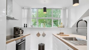 A modern kitchen with white cabinetry, a stainless steel sink, a coffee maker, and a window with curtains. - Beautiful home in Aabenraa with house sea view (Aabenraa)