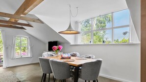A dining area with a wooden table, four grey chairs, a hanging light fixture, and a large window with a view of greenery. - Beautiful home in Aabenraa with house sea view (Aabenraa)