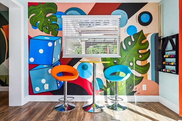 A room with a colorful abstract mural, a pool table, and two bar stools.