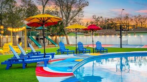 Ein Swimmingpool mit bunten Terrassenfliesen, blauen Liegestühlen und Sonnenschirmen.