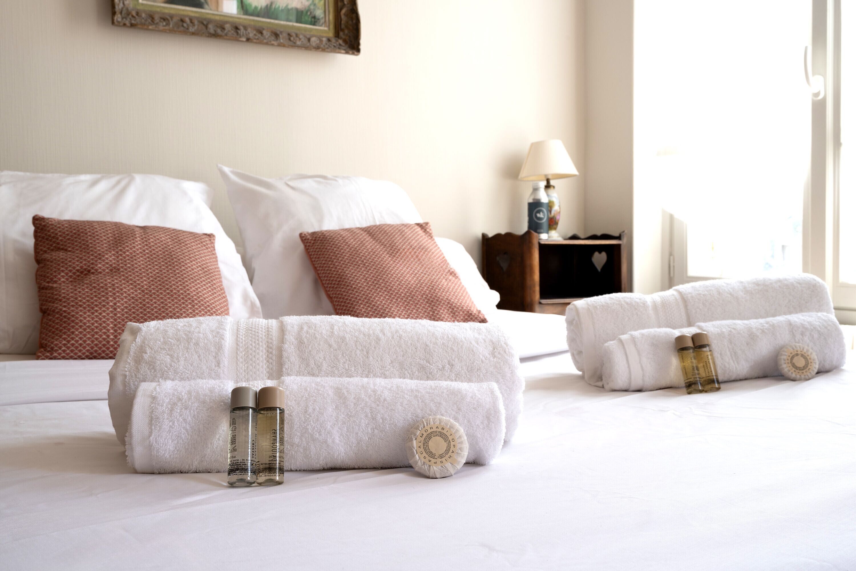 Ein ordentlich bezogenes Bett mit weißen und braunen Kissen, einer Lampe und zusammengerollten Handtüchern mit ätherischen Ölen in einem Hotelzimmer.