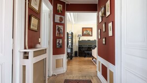 A hallway with red walls, white trim, and a patterned rug. There are framed pictures on the walls and a fireplace in the background.