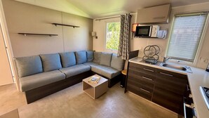 Ett kompakt vardagsrum med en soffa, ett litet soffbord, en liten köksdel med mikrovågsugn och ett fönster med persienner.